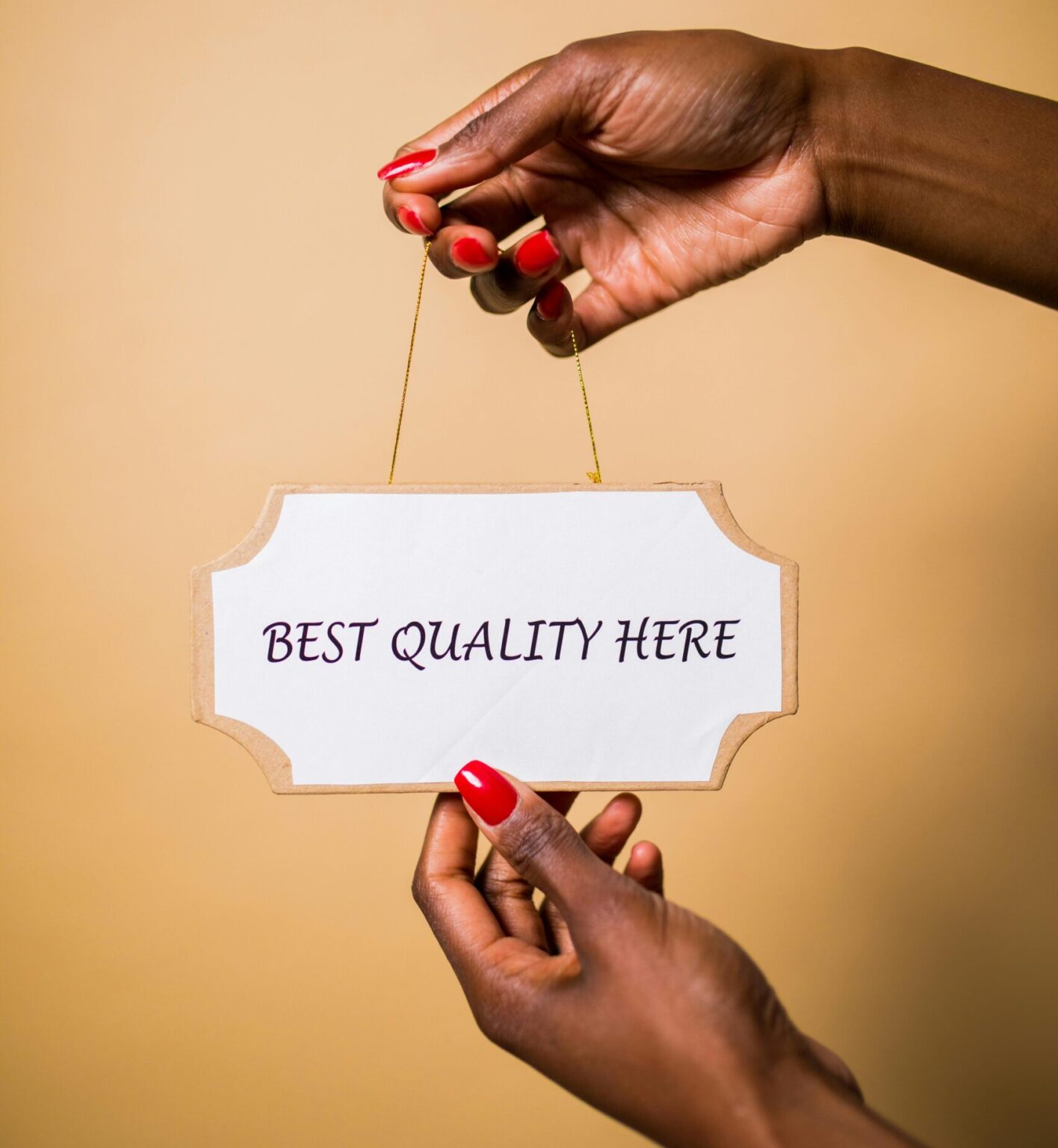 Stylish female hands with red nails holding a sign that says 'Best Quality Here' against a soft background.